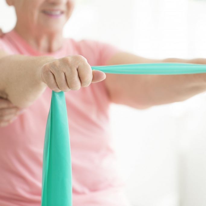 Senior woman holding a teal scarf in her hands while performing active pnf rehabilitation exercise with help of her therapist