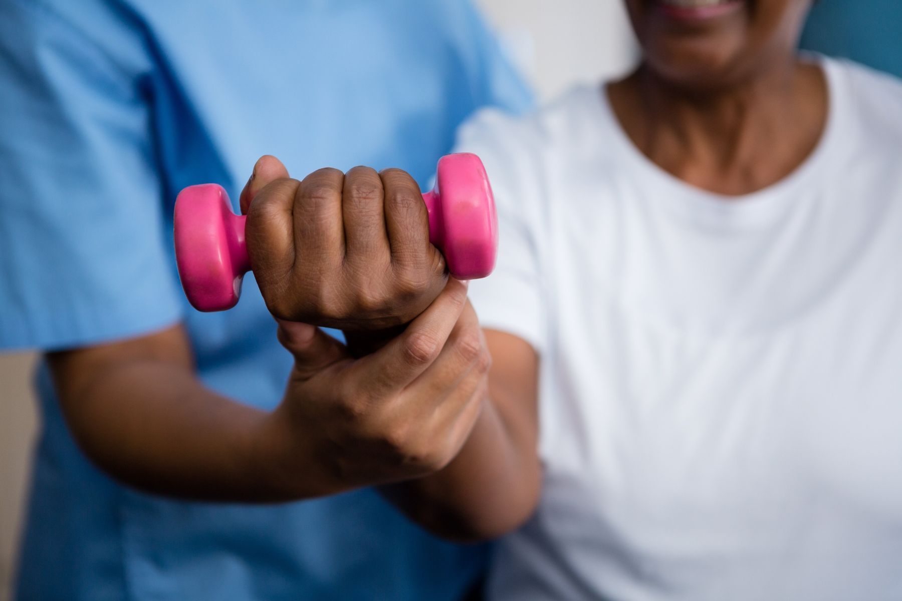 Midsection of nurse guiding senior woman in lifting dumbbell at retirement home